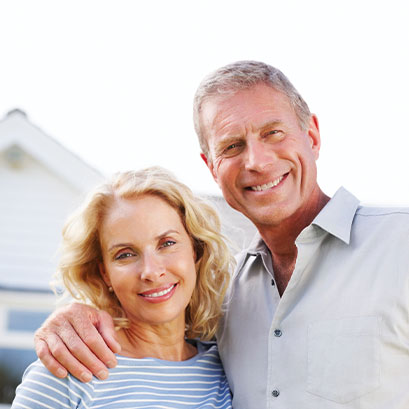 Photo of a couple in front of their house. Links to Gifts of Real Estate